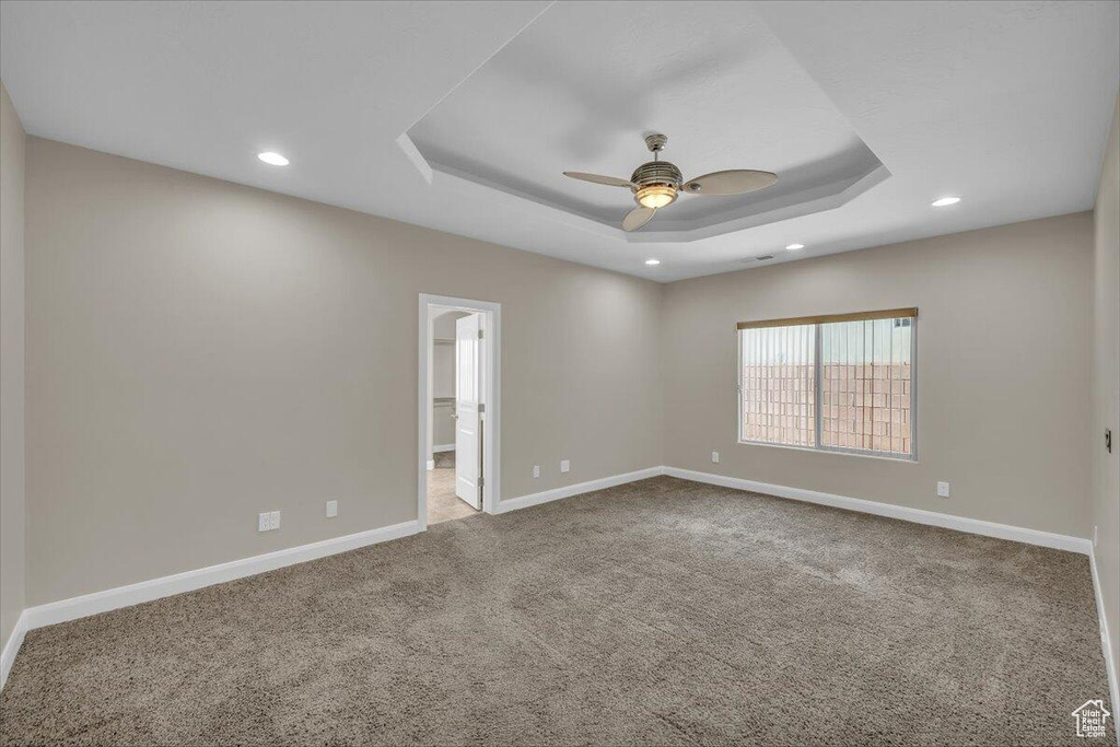 Empty room featuring carpet, baseboards, recessed lighting, a raised ceiling, and a ceiling fan