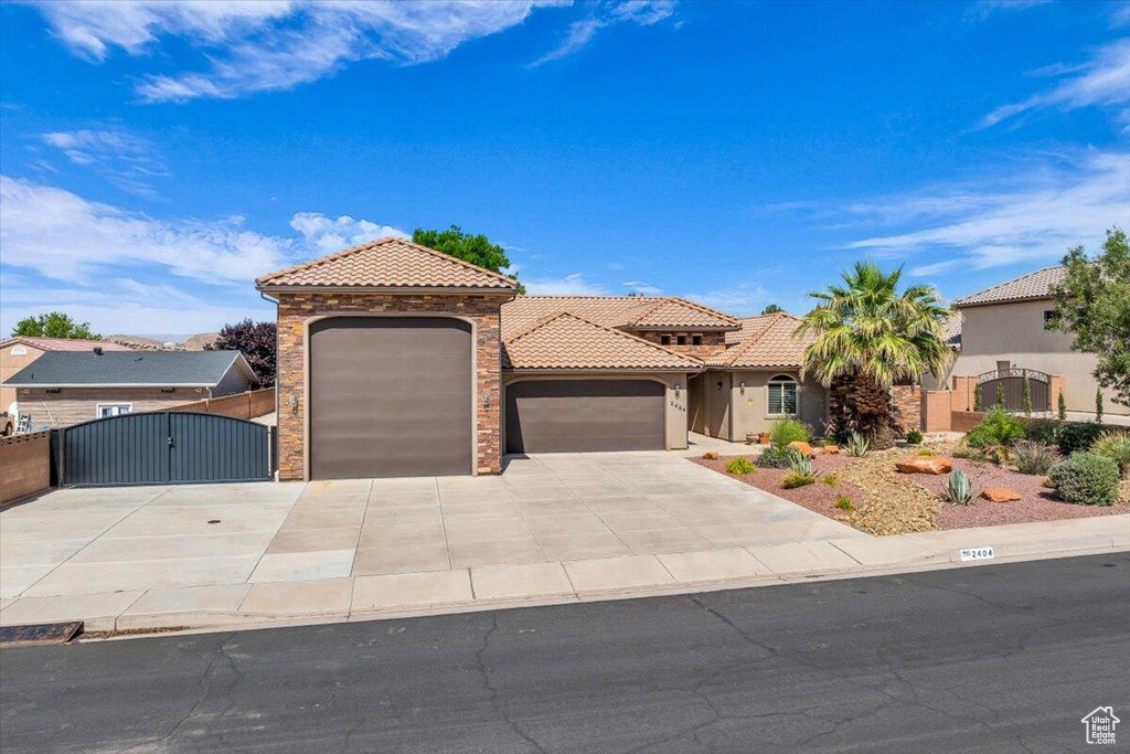 Mediterranean / spanish house featuring a gate, an attached garage, a tile roof, driveway, and stucco siding