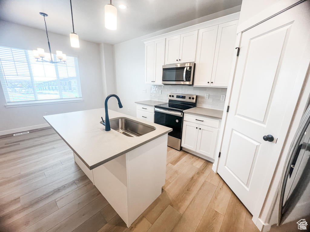 Kitchen featuring a sink, stainless steel appliances, a center island with sink, light countertops, and backsplash