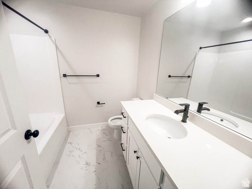 Bathroom featuring marble look tiles, vanity, baseboards,  shower combination, and toilet