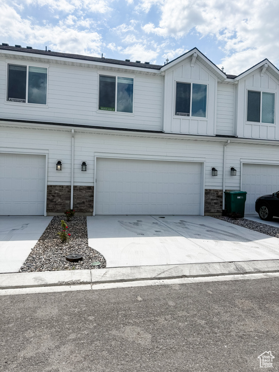 Multi unit property featuring stone siding, an attached garage, and driveway