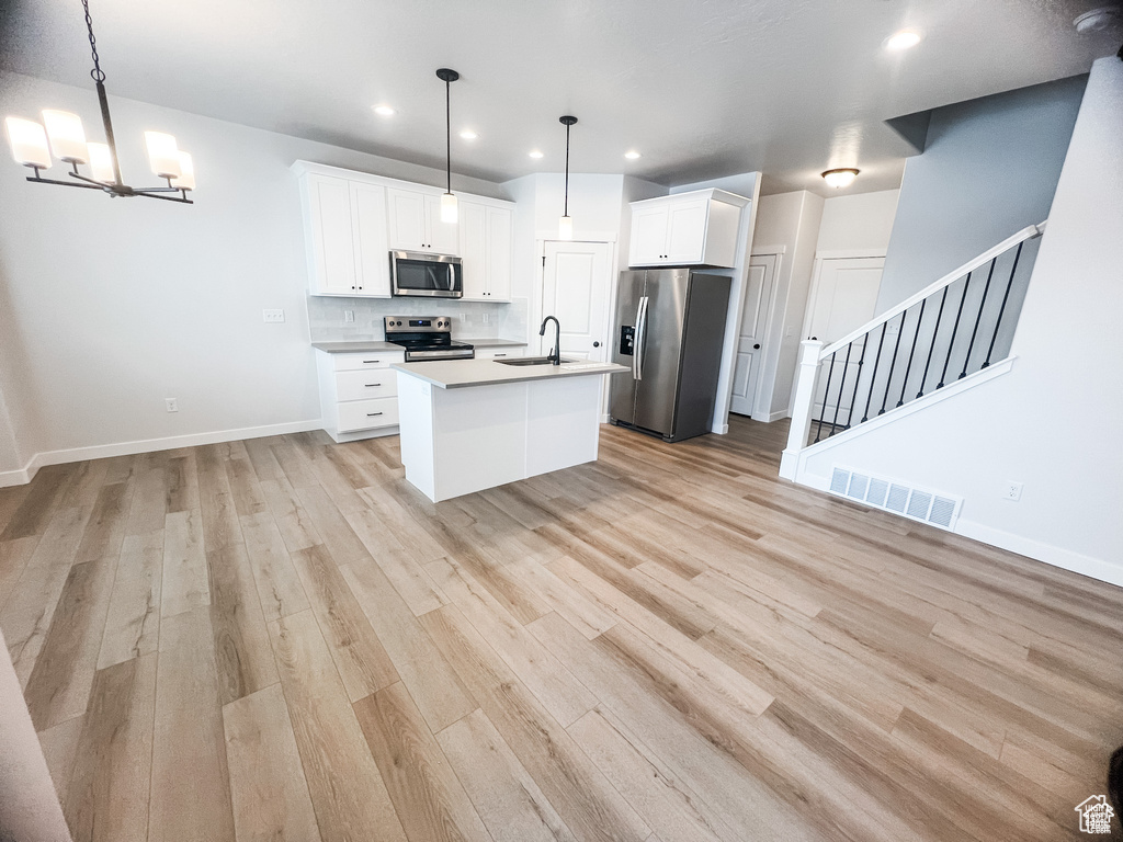 Kitchen with appliances with stainless steel finishes, a sink, light wood-style floors, white cabinets, and recessed lighting
