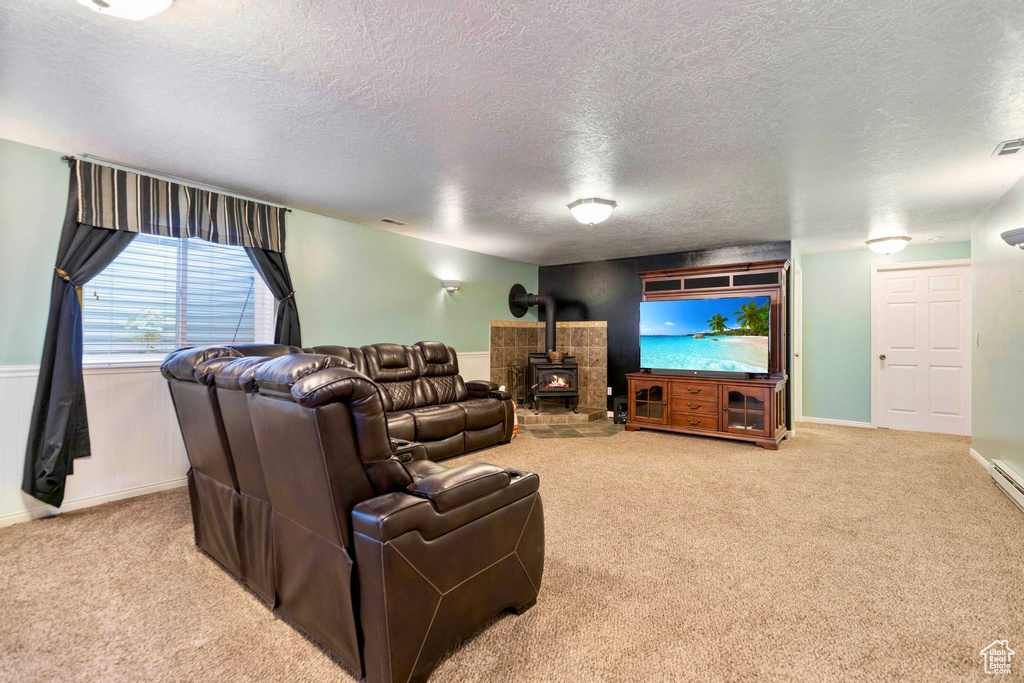 Living area with a textured ceiling, carpet flooring, a wood stove, and baseboards