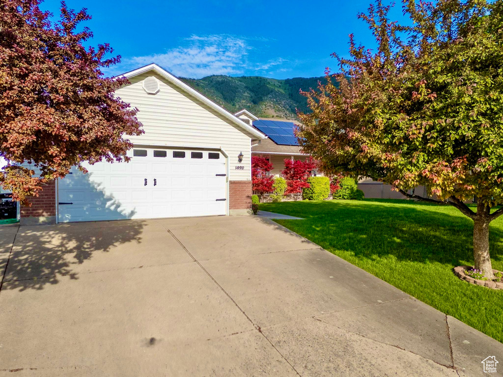 View of front of property with a mountain view, a front lawn, driveway, brick siding, and an attached garage