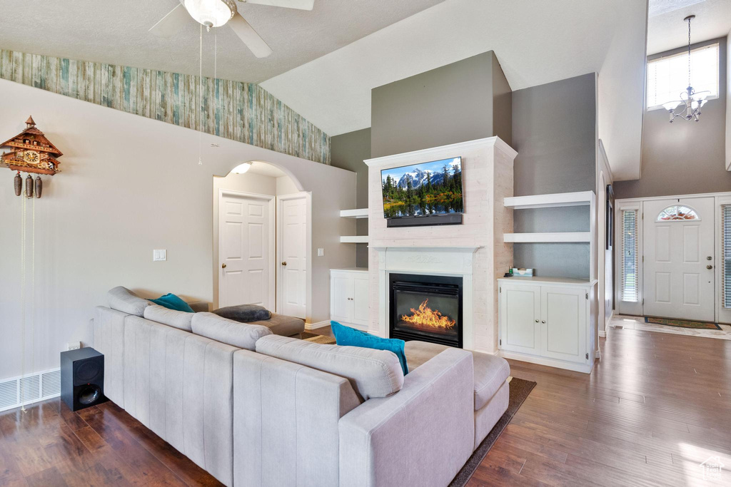 Living room with high vaulted ceiling, dark wood-style flooring, ceiling fan, a glass covered fireplace, and arched walkways