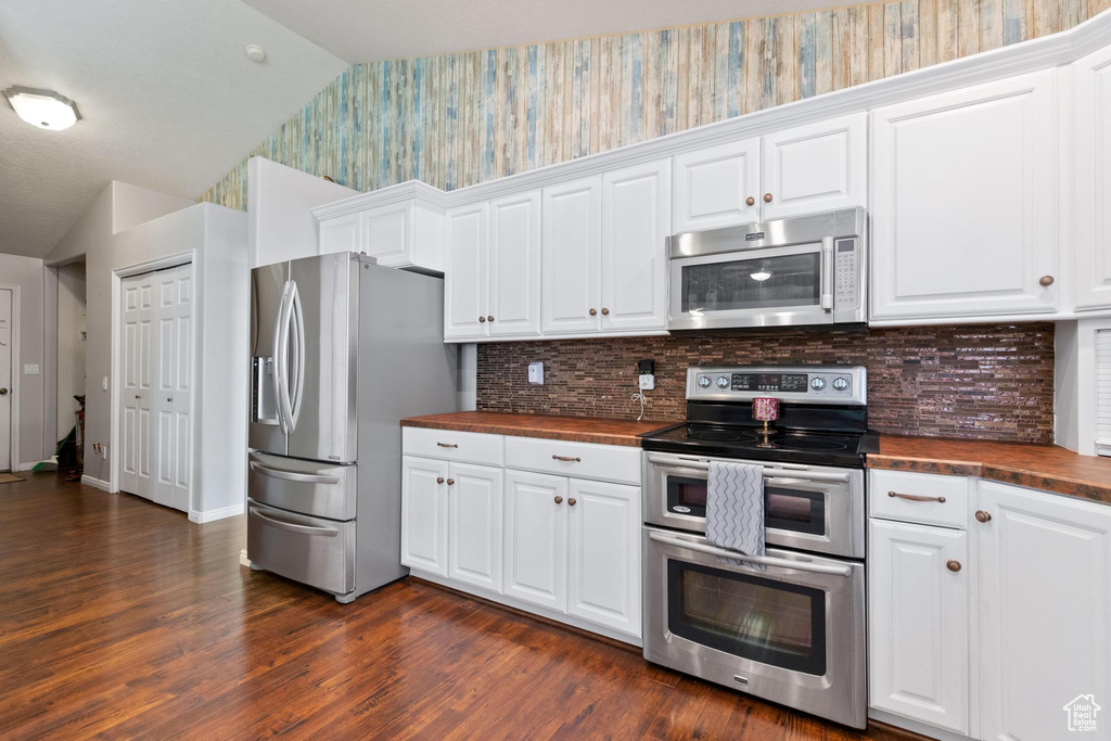 Kitchen featuring stainless steel appliances, wallpapered walls, butcher block counters, vaulted ceiling, and dark wood finished floors