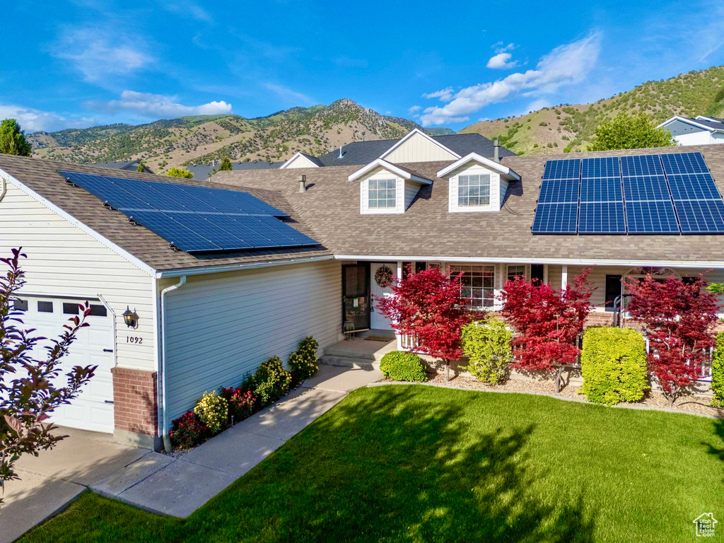 View of front of house with a mountain view, solar panels, a front yard, and roof with shingles