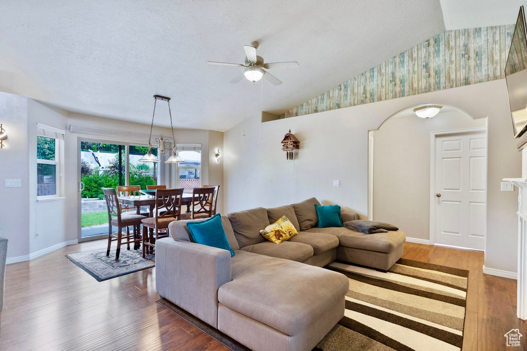 Living area with a ceiling fan, wallpapered walls, wood finished floors, baseboards, and lofted ceiling