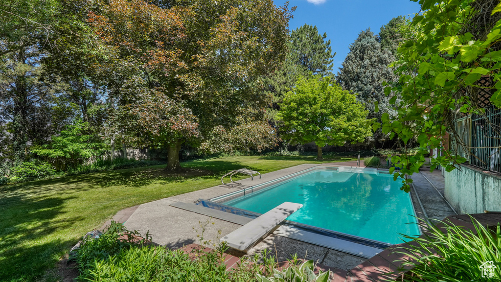 Outdoor pool with a yard, a diving board, and view of scattered trees