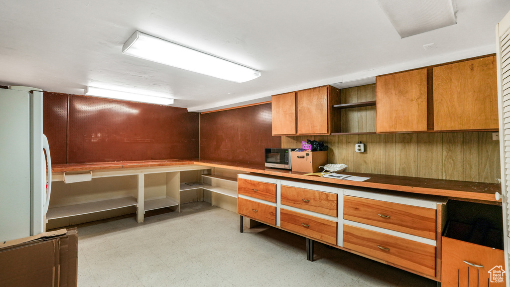 Kitchen featuring freestanding refrigerator, open shelves, brown cabinetry, light floors, and wood walls