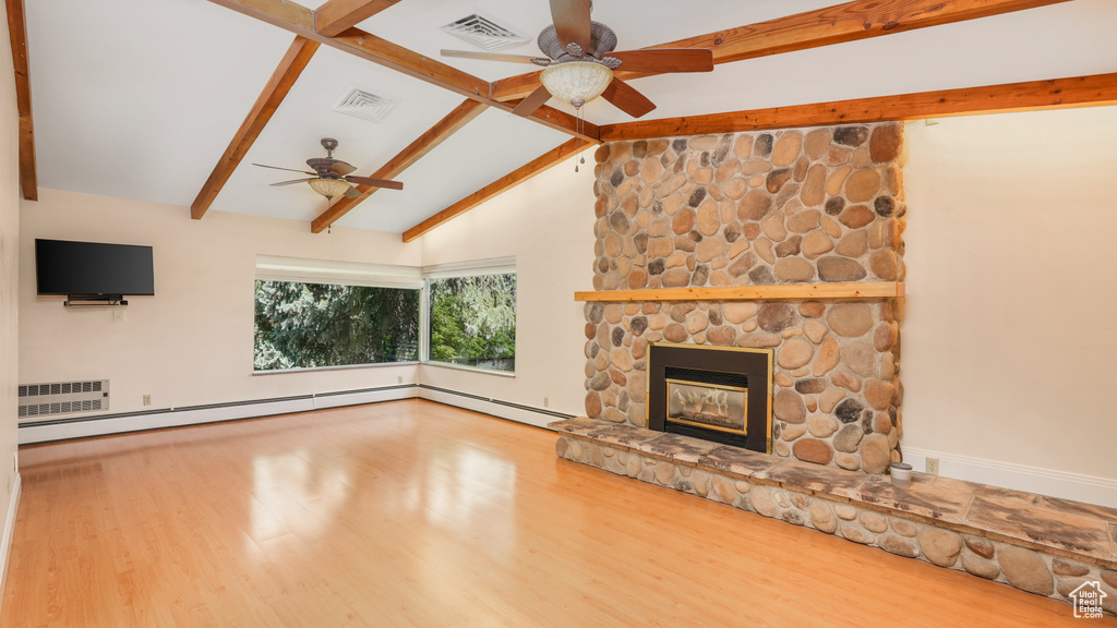 Unfurnished living room with ceiling fan, wood finished floors, a stone fireplace, baseboards, and a baseboard radiator