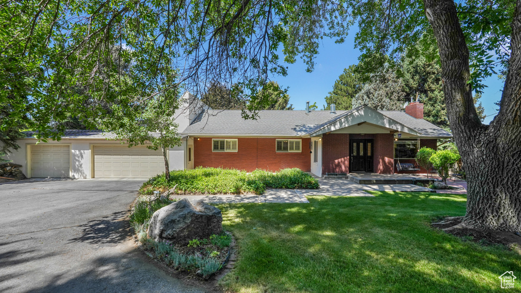 Ranch-style home with driveway, a front yard, a garage, brick siding, and a chimney