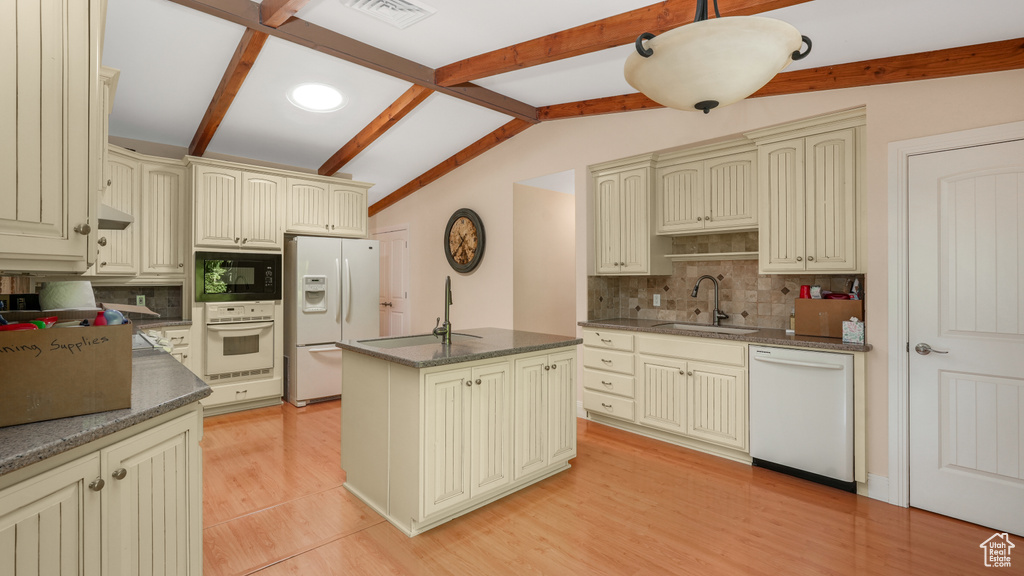 Kitchen featuring cream cabinetry, white appliances, and tasteful backsplash