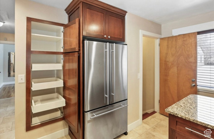 Kitchen featuring stainless steel refrigerator, light stone counters, baseboards, and healthy amount of natural light