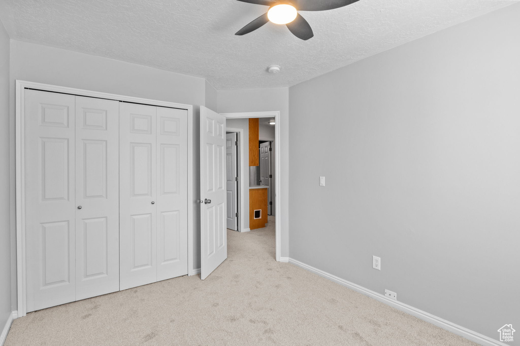 Unfurnished bedroom featuring carpet flooring, a textured ceiling, baseboards, a closet, and ceiling fan