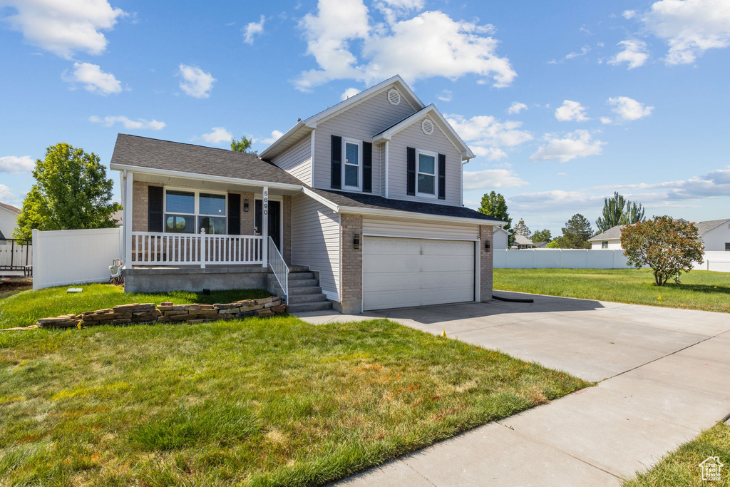 Tri-level home featuring covered porch, driveway, a garage, and brick siding