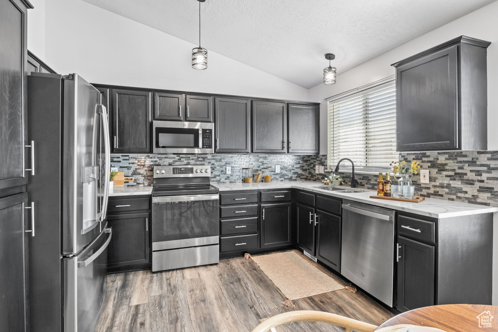 Kitchen with appliances with stainless steel finishes, lofted ceiling, backsplash, a textured ceiling, and light wood-style flooring