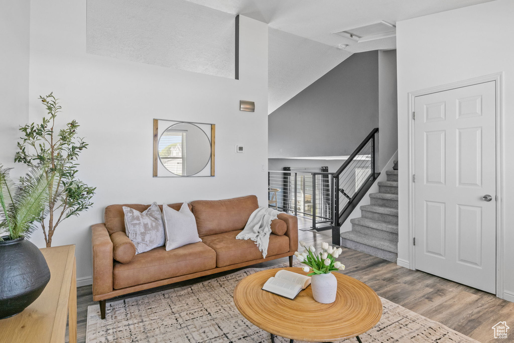 Living room featuring wood finished floors, attic access, high vaulted ceiling, baseboards, and stairs