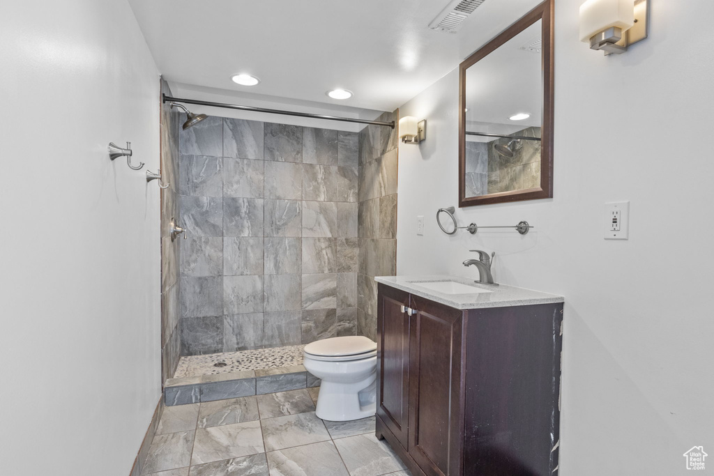 Bathroom with toilet, recessed lighting, a tile shower, vanity, and marble finish flooring