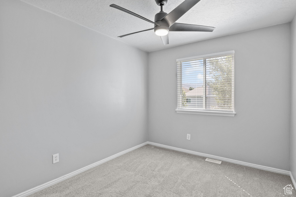 Carpeted spare room featuring a ceiling fan, a textured ceiling, and baseboards