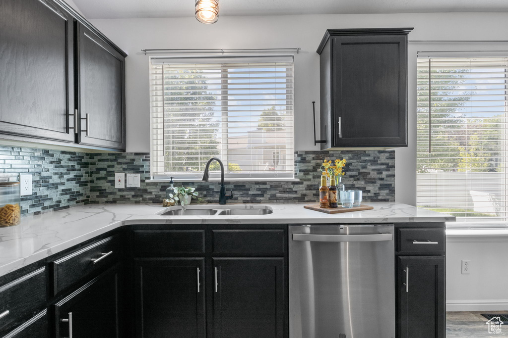 Kitchen featuring stainless steel dishwasher, a sink, tasteful backsplash, and light stone counters