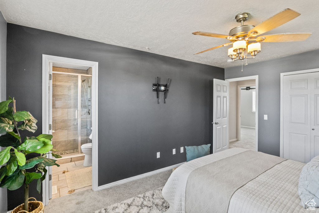 Carpeted bedroom with baseboards, a ceiling fan, ensuite bathroom, and a textured ceiling
