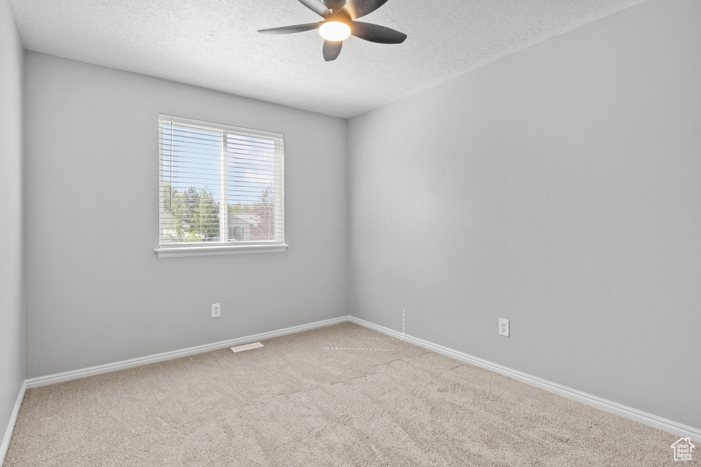 Spare room featuring a textured ceiling, a ceiling fan, carpet floors, and baseboards