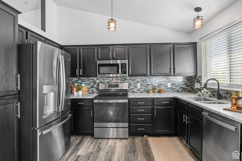 Kitchen with appliances with stainless steel finishes, vaulted ceiling, a sink, backsplash, and wood finished floors