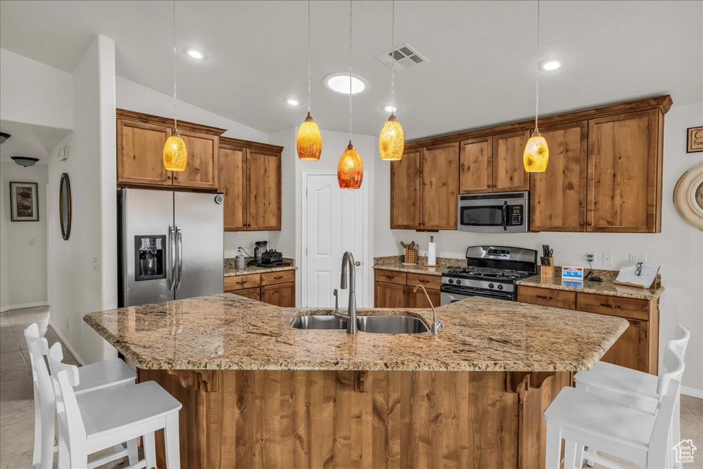 Kitchen featuring stainless steel appliances, a sink, brown cabinetry, a kitchen breakfast bar, and lofted ceiling
