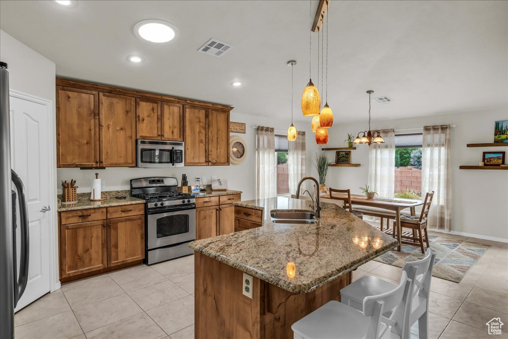 Kitchen featuring appliances with stainless steel finishes, a sink, brown cabinetry, a kitchen breakfast bar, and light tile patterned flooring