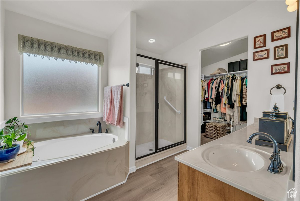 Full bathroom with a shower stall, wood finished floors, a bath, vanity, and a spacious closet