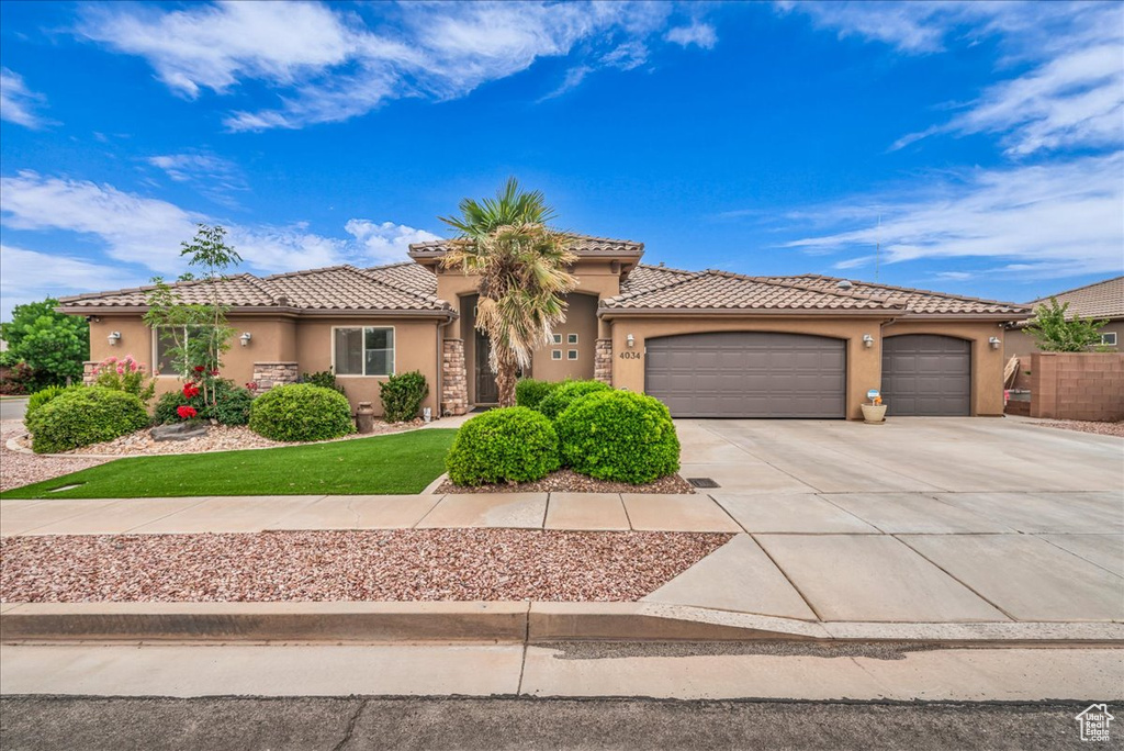 Mediterranean / spanish-style house featuring stucco siding, driveway, a garage, a tiled roof, and a front lawn