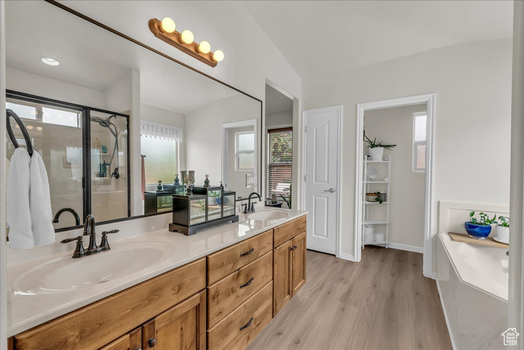 Full bath with double vanity, wood finished floors, a garden tub, and a stall shower