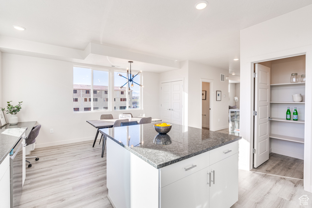 Kitchen with light wood-style flooring, a chandelier, white cabinets, pendant lighting, and dark stone countertops