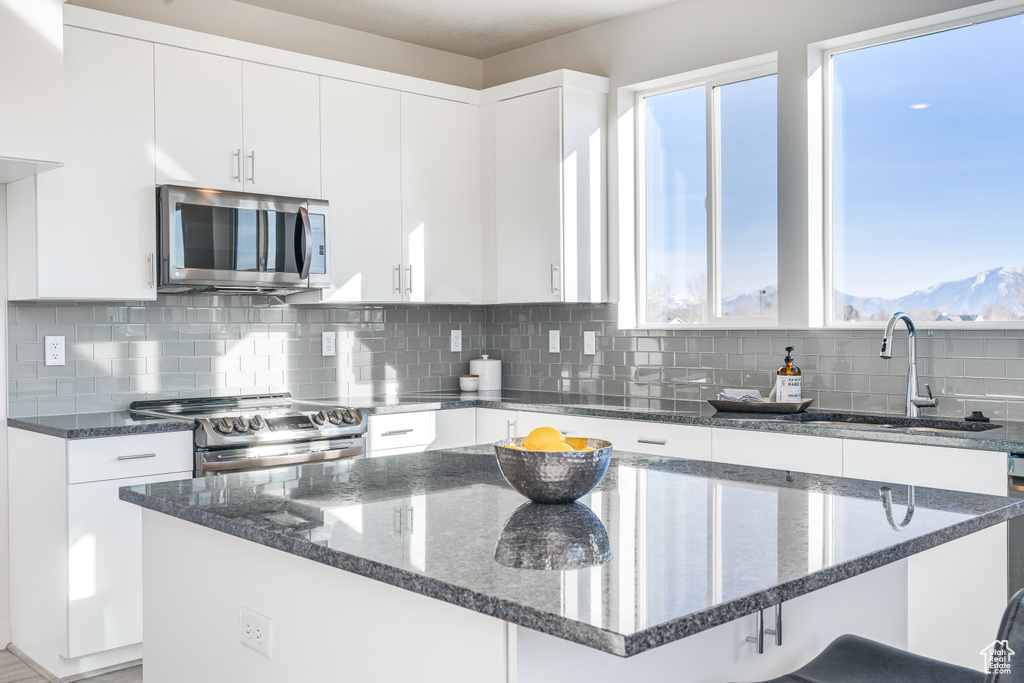Kitchen with appliances with stainless steel finishes, a sink, healthy amount of natural light, and dark stone counters
