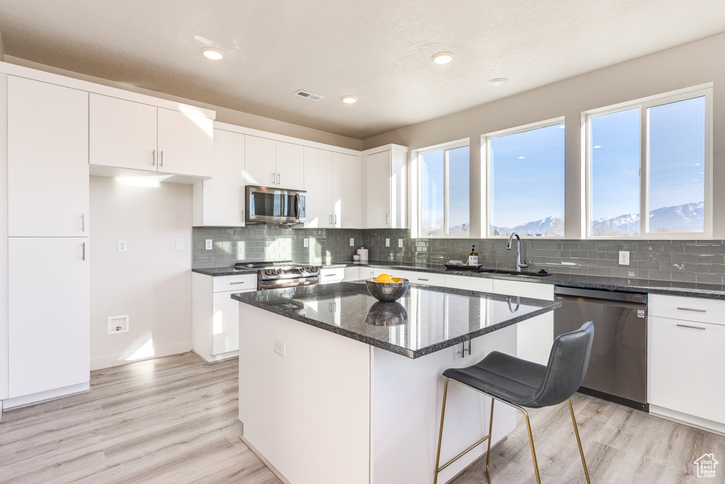 Kitchen with appliances with stainless steel finishes, dark stone countertops, light wood-style floors, white cabinets, and recessed lighting