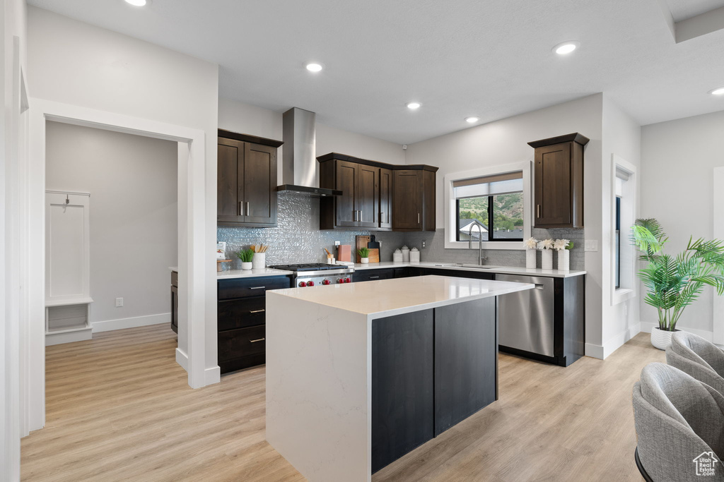 Kitchen with dishwasher, wall chimney range hood, a sink, dark brown cabinetry, and a center island