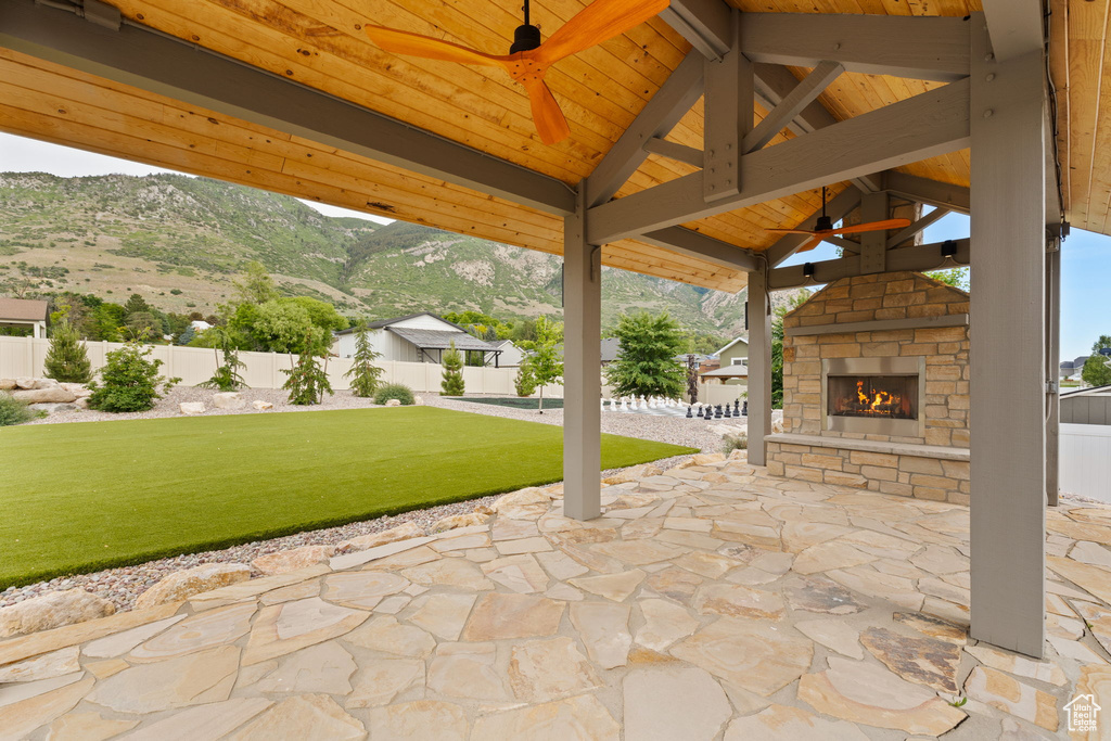 View of patio featuring an outdoor stone fireplace, a ceiling fan, a gazebo, and a mountain view