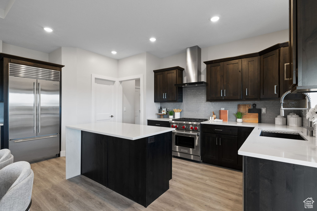 Kitchen with premium appliances, wall chimney range hood, a sink, backsplash, and light countertops