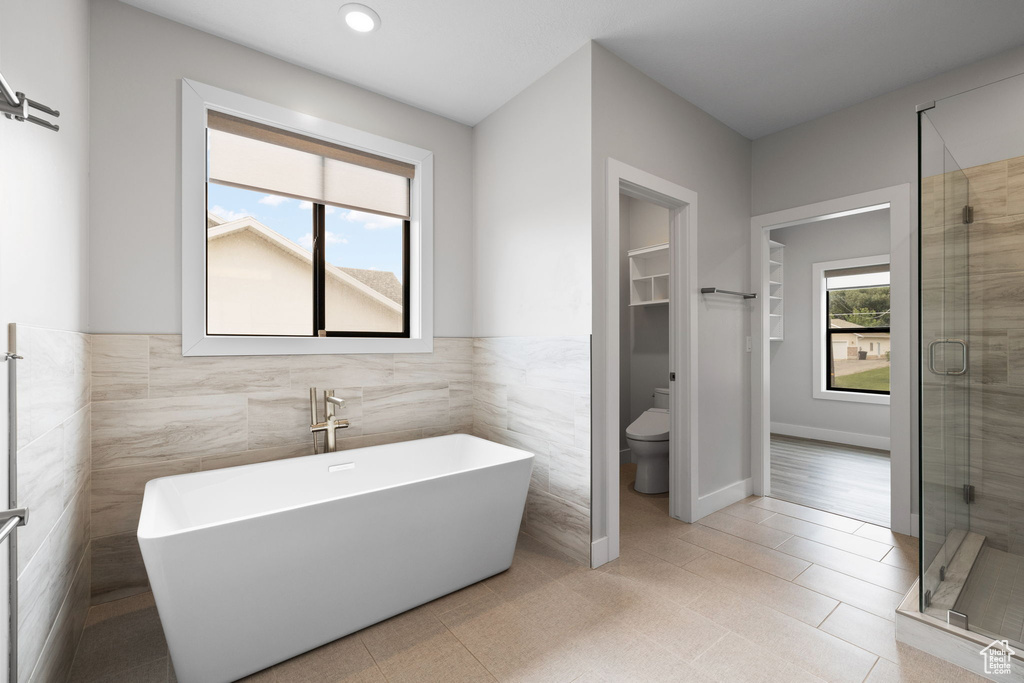 Bathroom featuring tile walls, a freestanding tub, toilet, a stall shower, and wainscoting