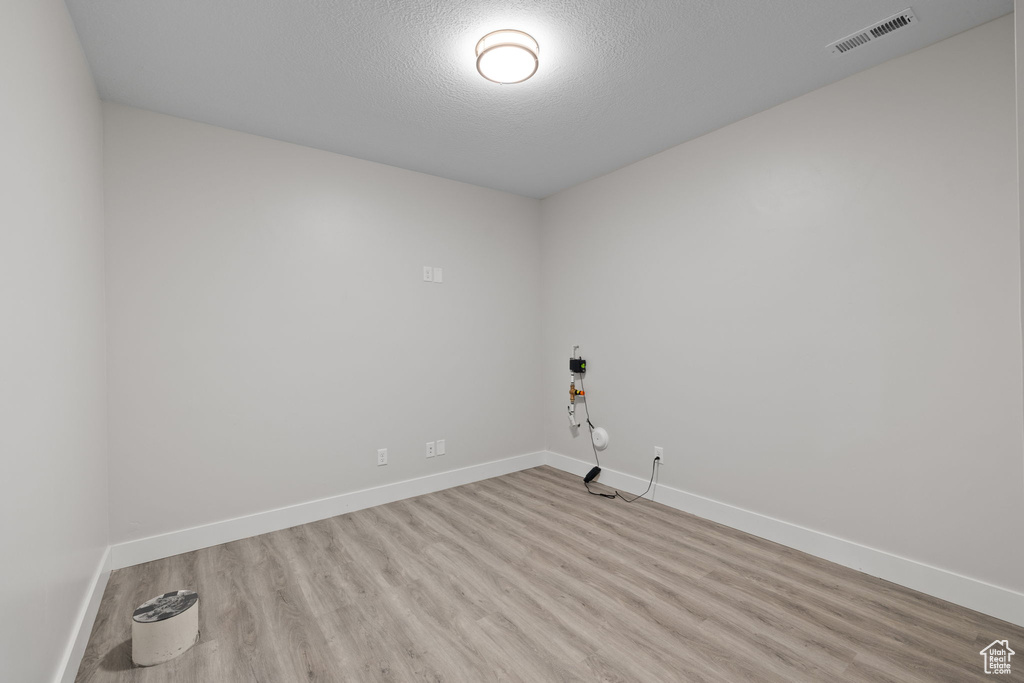 Unfurnished room with light wood-type flooring, baseboards, and a textured ceiling