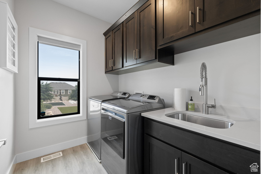 Laundry room featuring washing machine and clothes dryer, cabinet space, light wood-type flooring, and baseboards