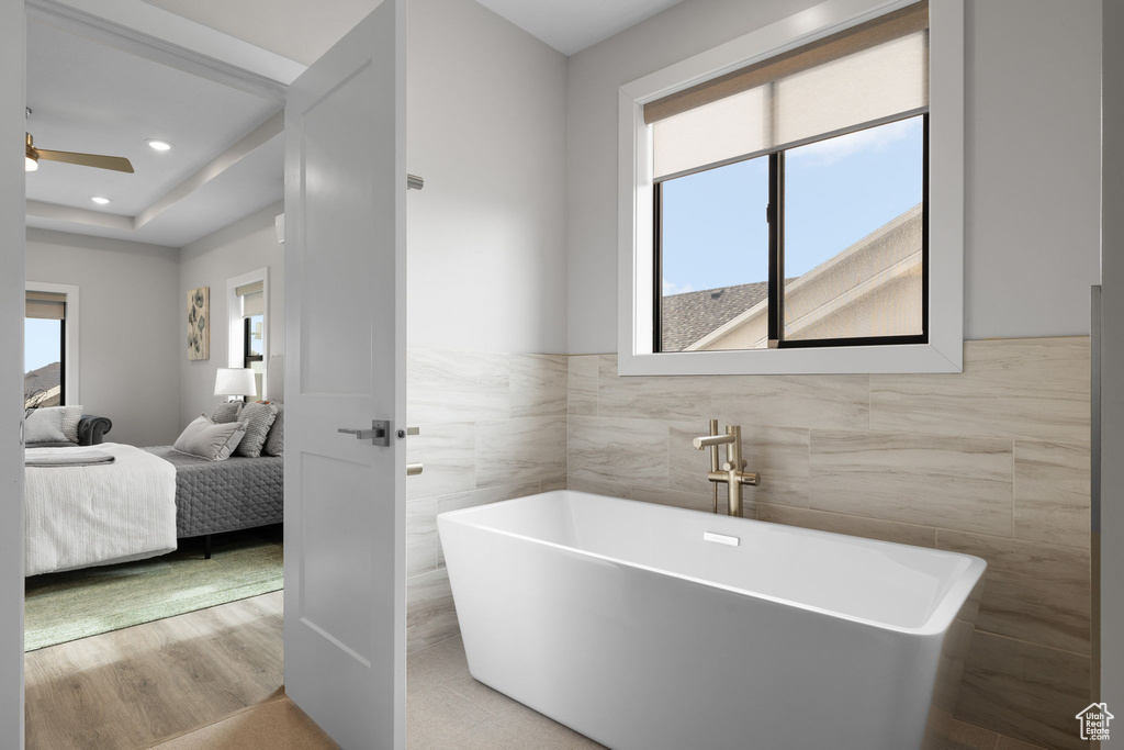Bathroom with tile walls, ensuite bathroom, a soaking tub, ceiling fan, and wainscoting