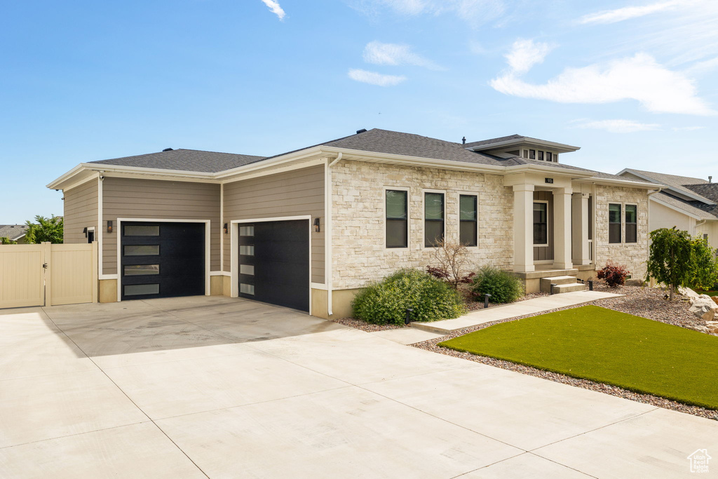 Prairie-style house with stone siding, an attached garage, a gate, and driveway