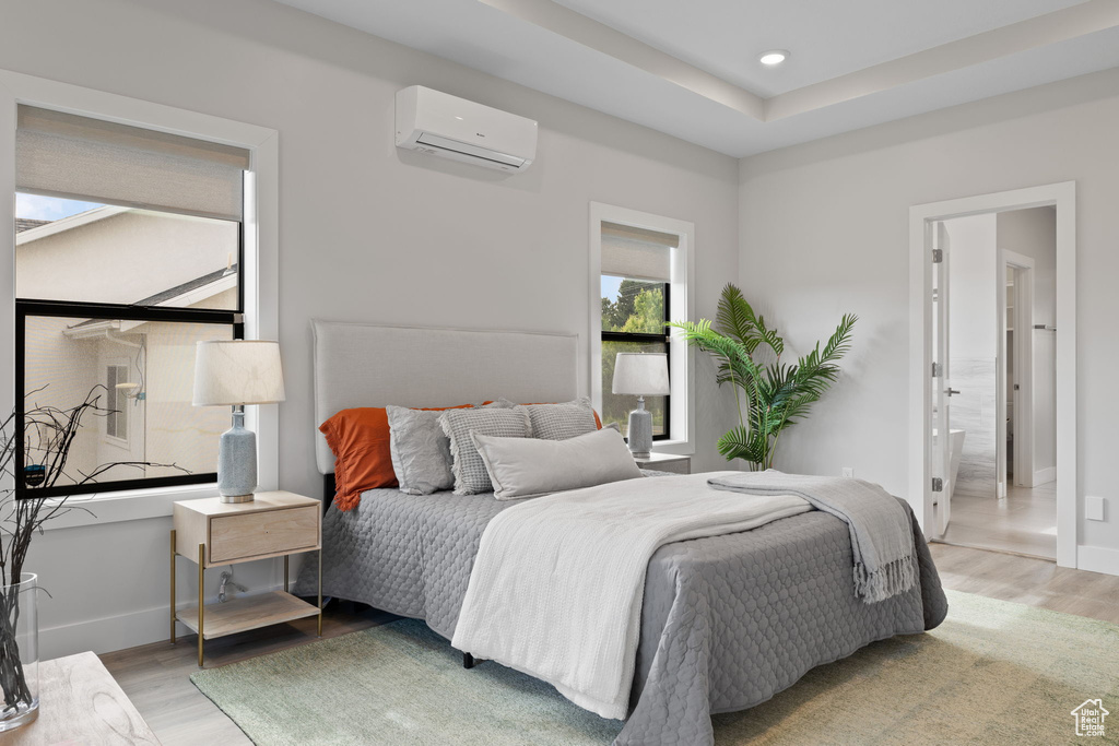 Bedroom with an AC wall unit, light wood-style flooring, recessed lighting, baseboards, and connected bathroom