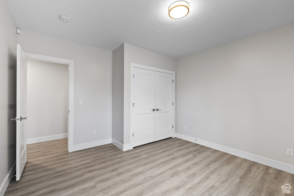 Unfurnished bedroom with light wood-type flooring, a closet, baseboards, and a textured ceiling