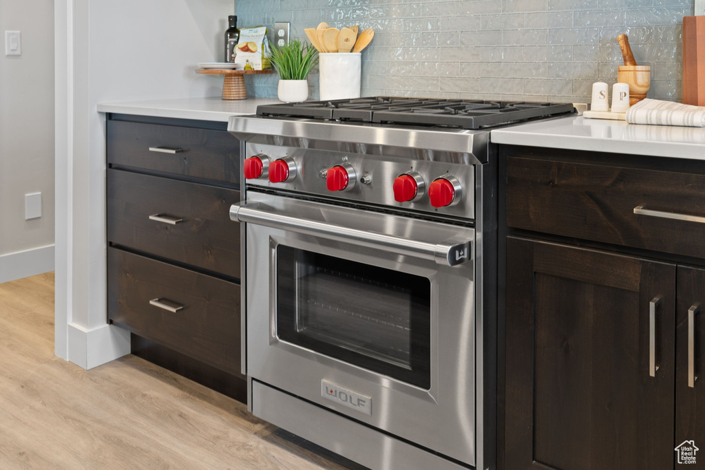 Kitchen with designer range, light wood-style flooring, light countertops, backsplash, and dark brown cabinets