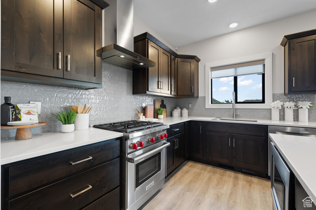 Kitchen featuring wall chimney exhaust hood, designer range, a sink, light countertops, and dark brown cabinetry