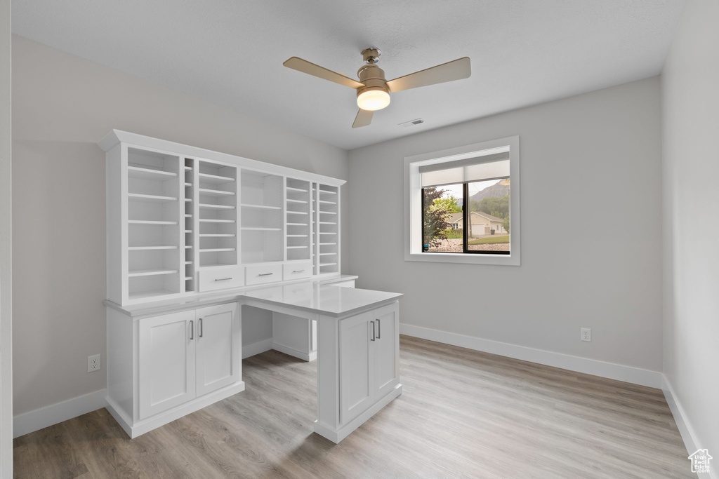 Unfurnished office with a ceiling fan, light wood-type flooring, and baseboards