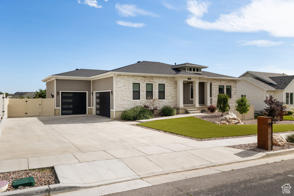 Prairie-style home featuring a gate, an attached garage, concrete driveway, stone siding, and a shingled roof